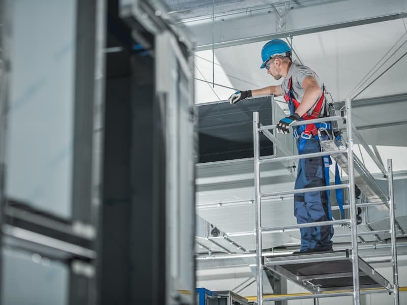 HVAC technician installing commercial air conditioning system on scaffolding