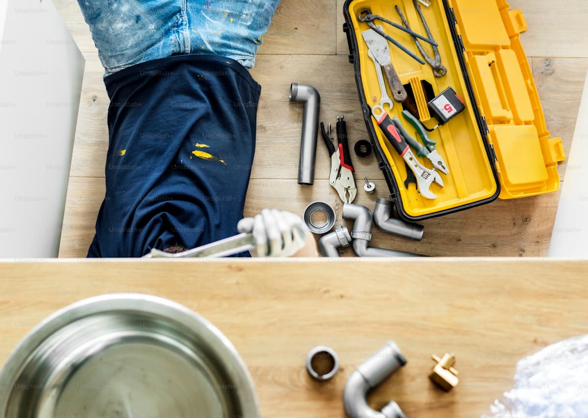 Plumber fixing kitchen sink pipes — emergency plumbing service call